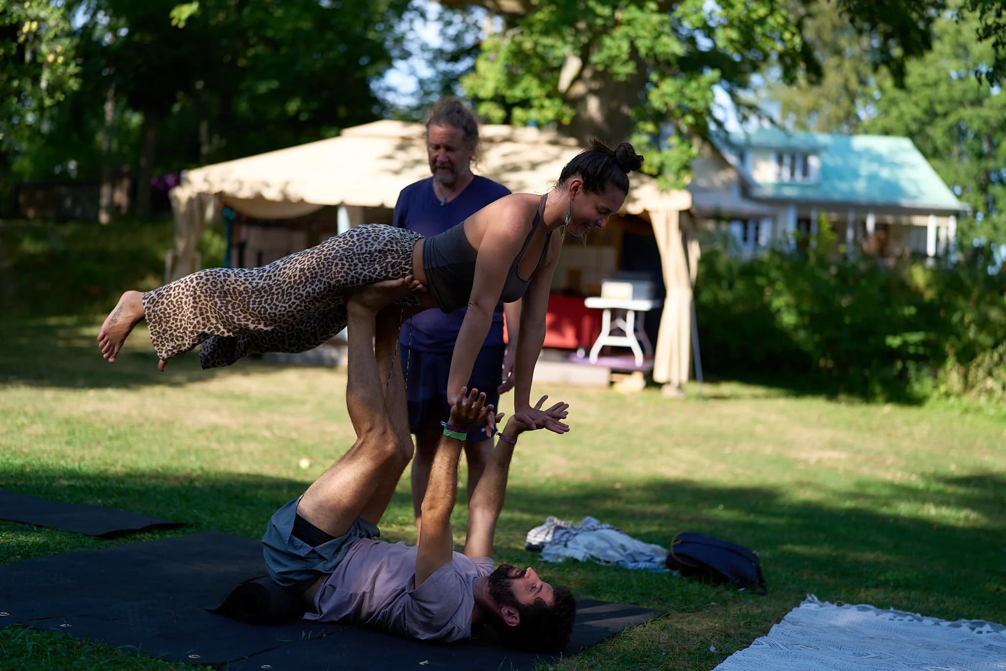 Two participants practising an acrobatic balance on the lawn, with a third standing nearby.