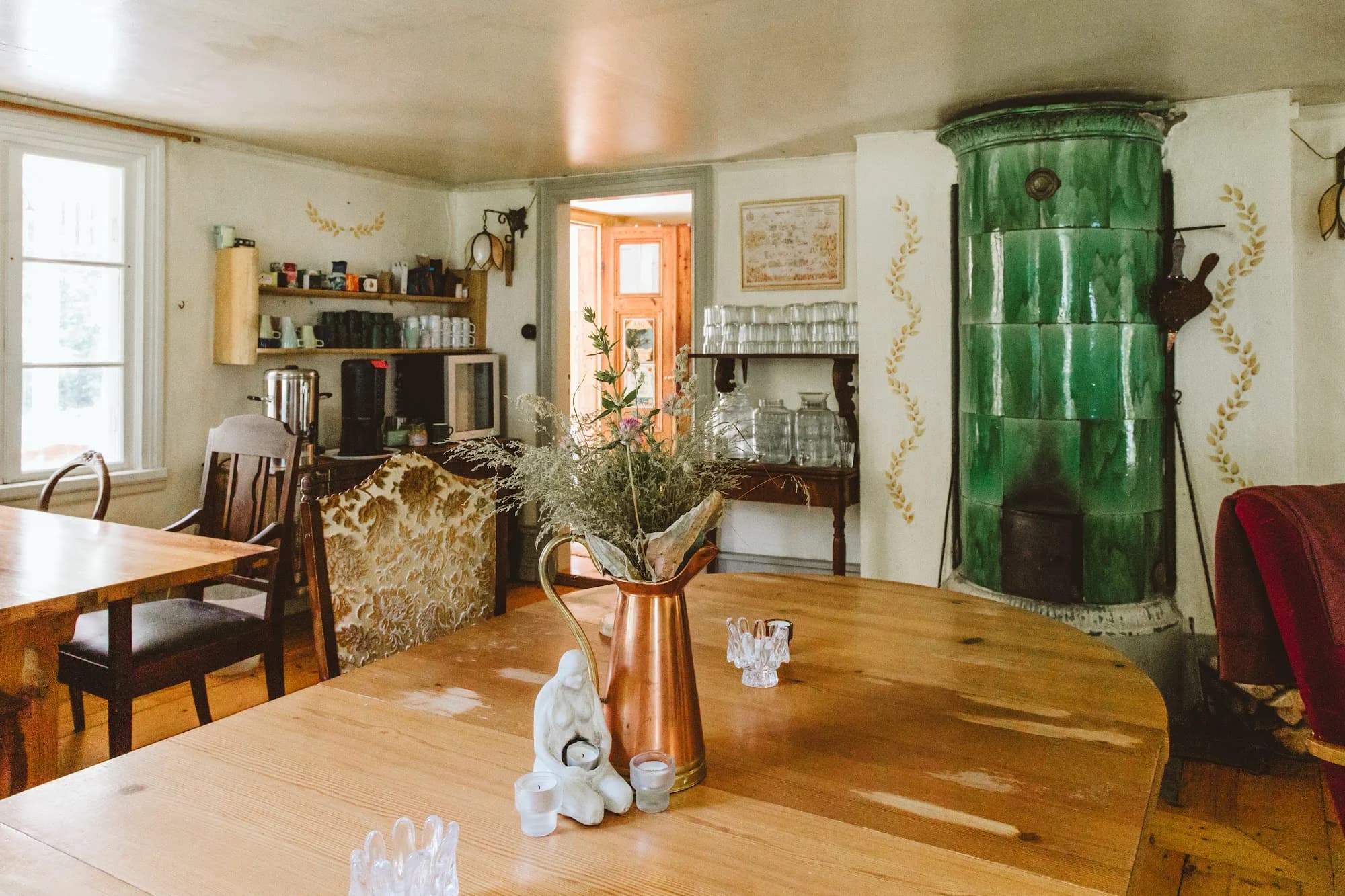 A green tiled stove and long wooden table inside the Main House