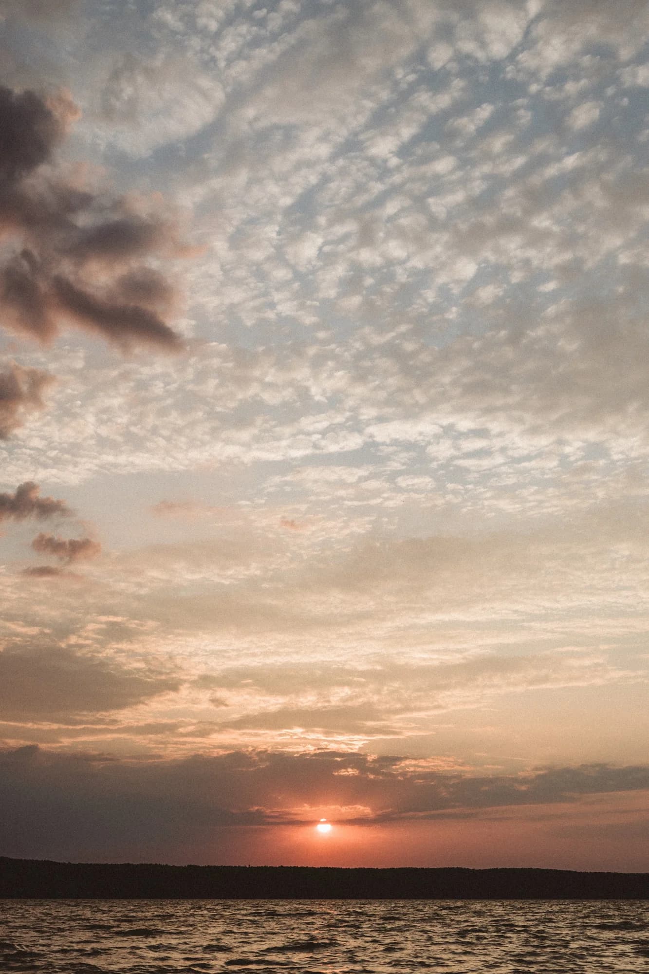 The sun setting under a sky of small clouds