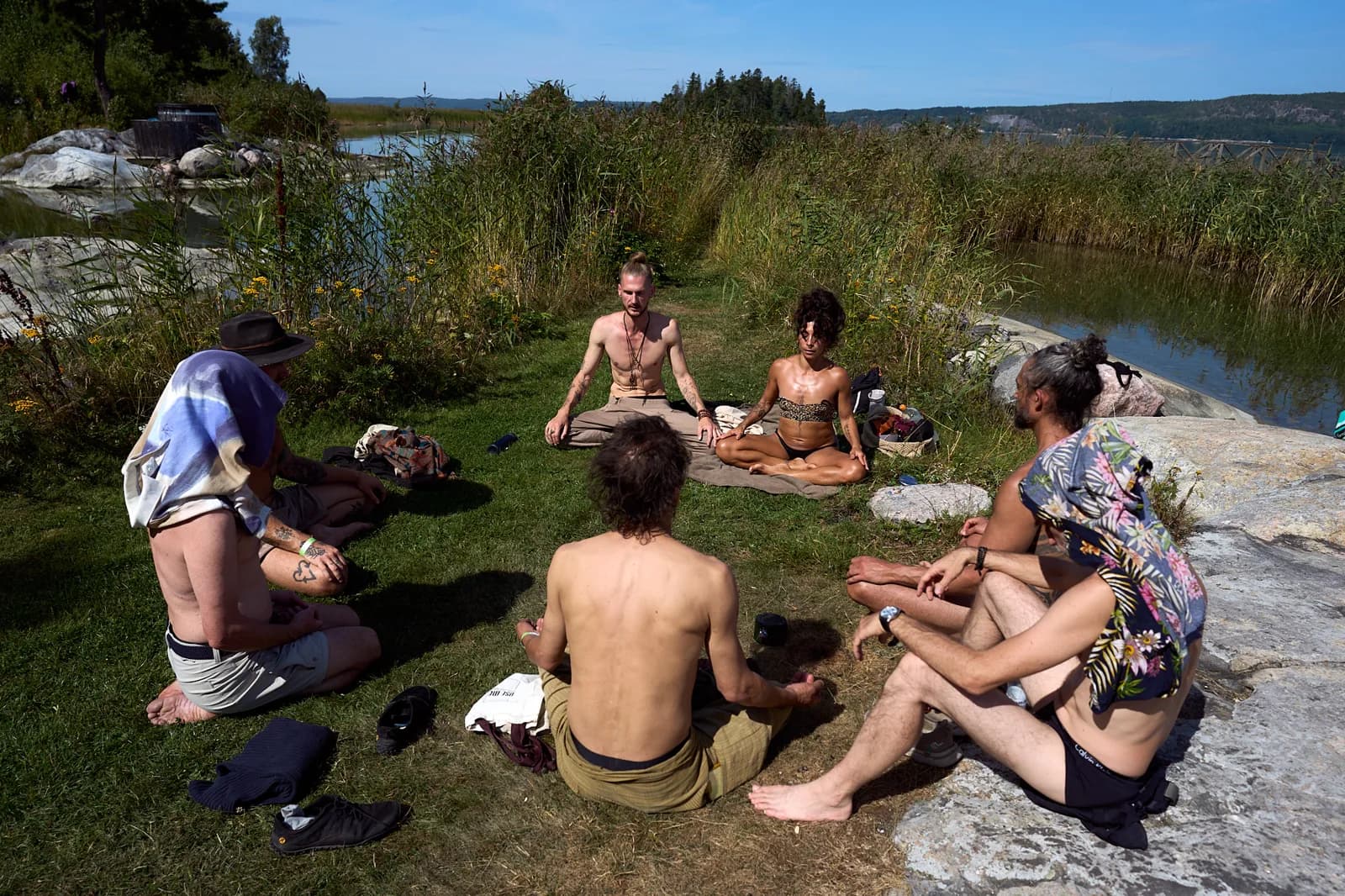 People sitting together in a circle on the grass by the water
