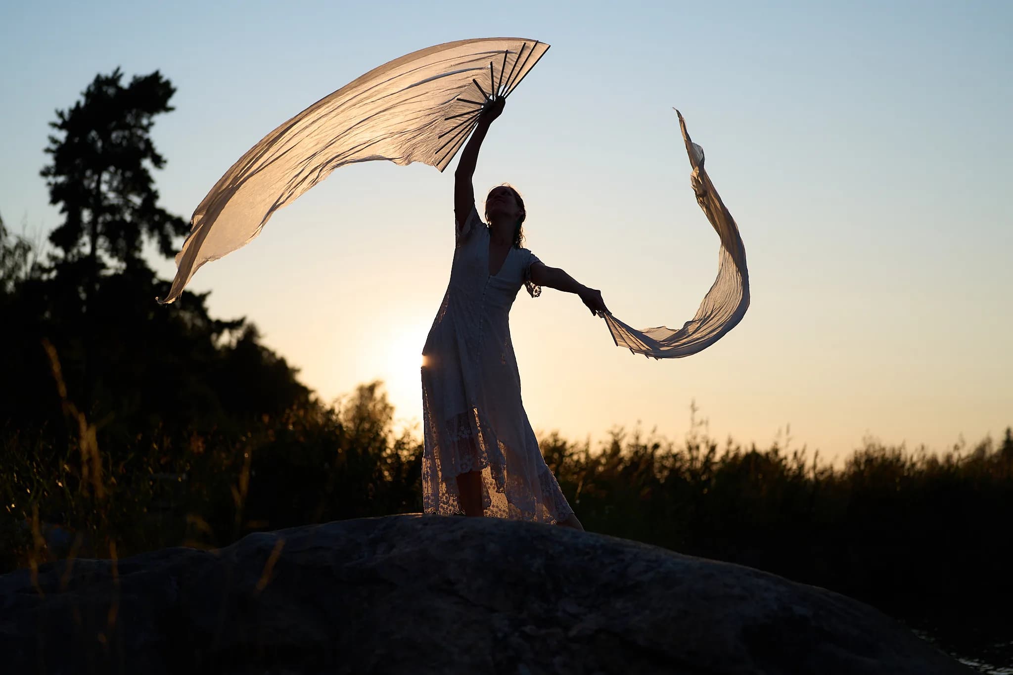 A dancer holding silk fans against the evening sky